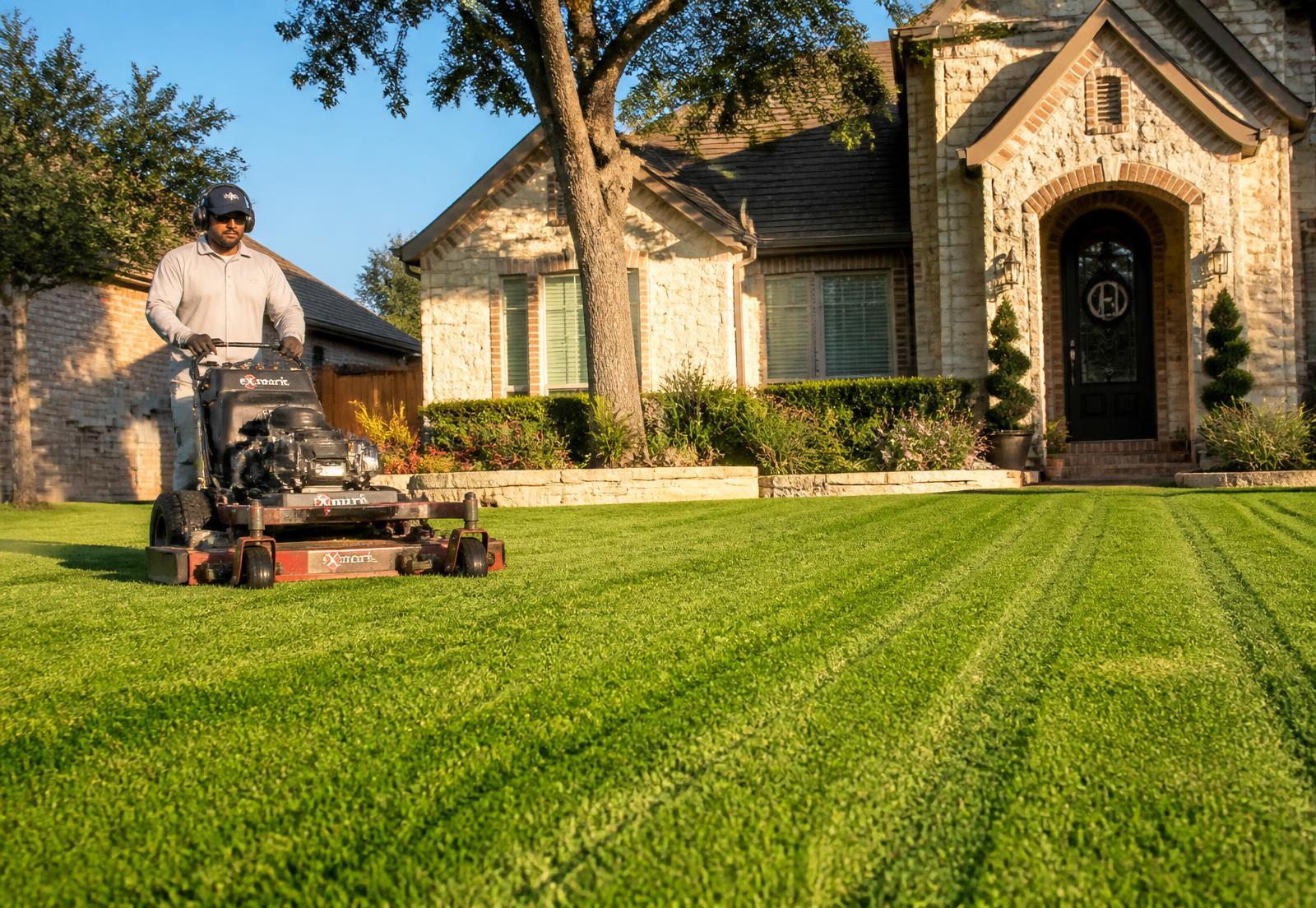 Freshly mowed green front lawn at a San Antonio home with a lawn care professional using a commercial mower